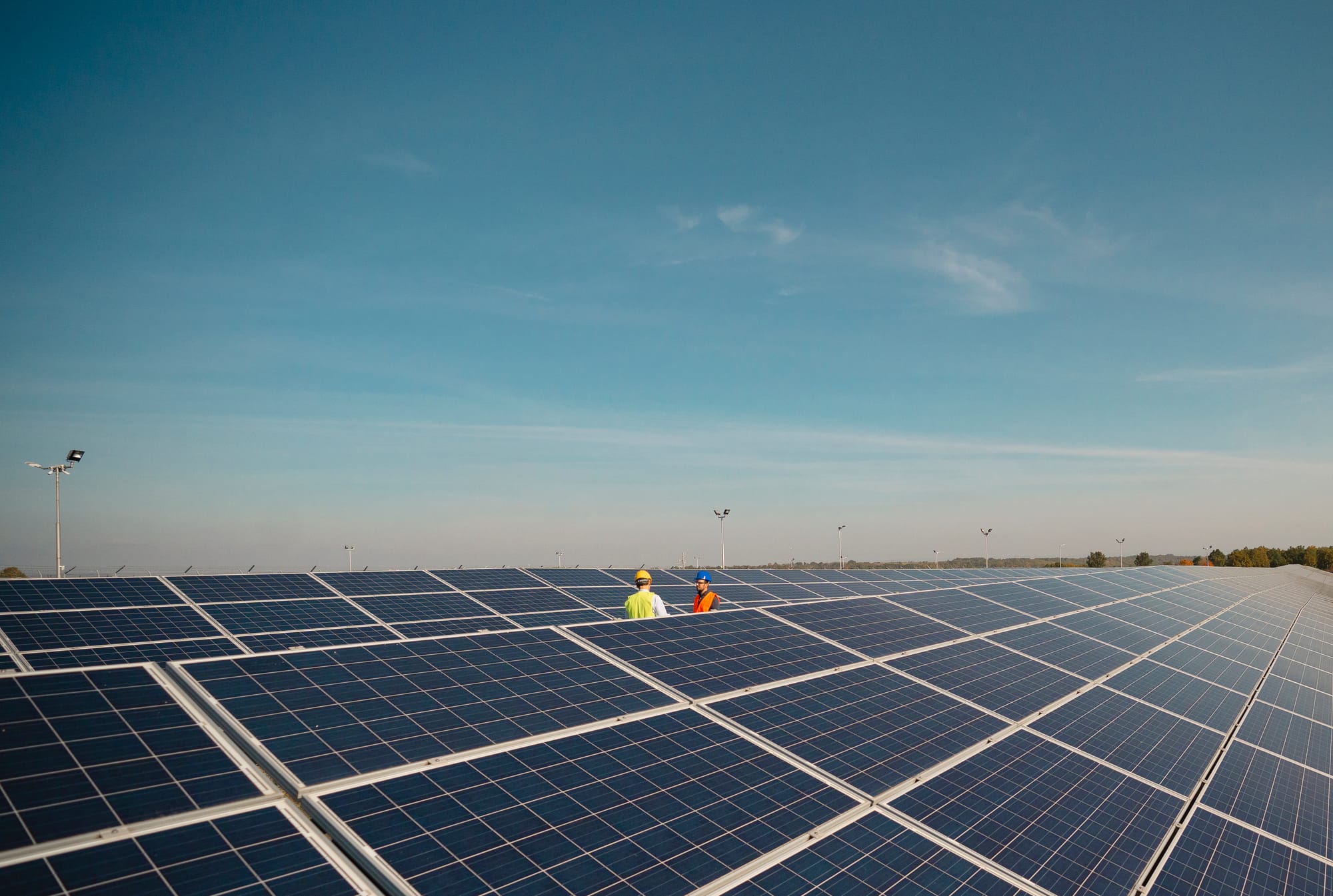 Dois engenheiros de campo, com colete de segurança, caminhando entre as fileiras de uma grande usina solar fotovoltaica.